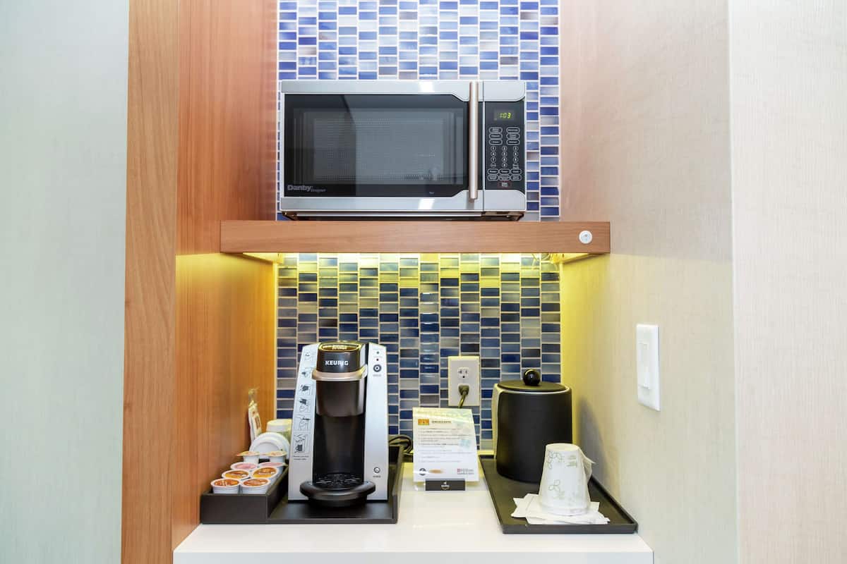Una kitchenette compacta equipada con microondas, cafetera y dispensador de té.