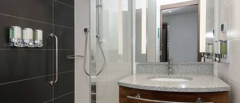 A modern bathroom with a granite countertop sink, a wooden vanity, a glass shower enclosure, and a mirror with a wooden frame.