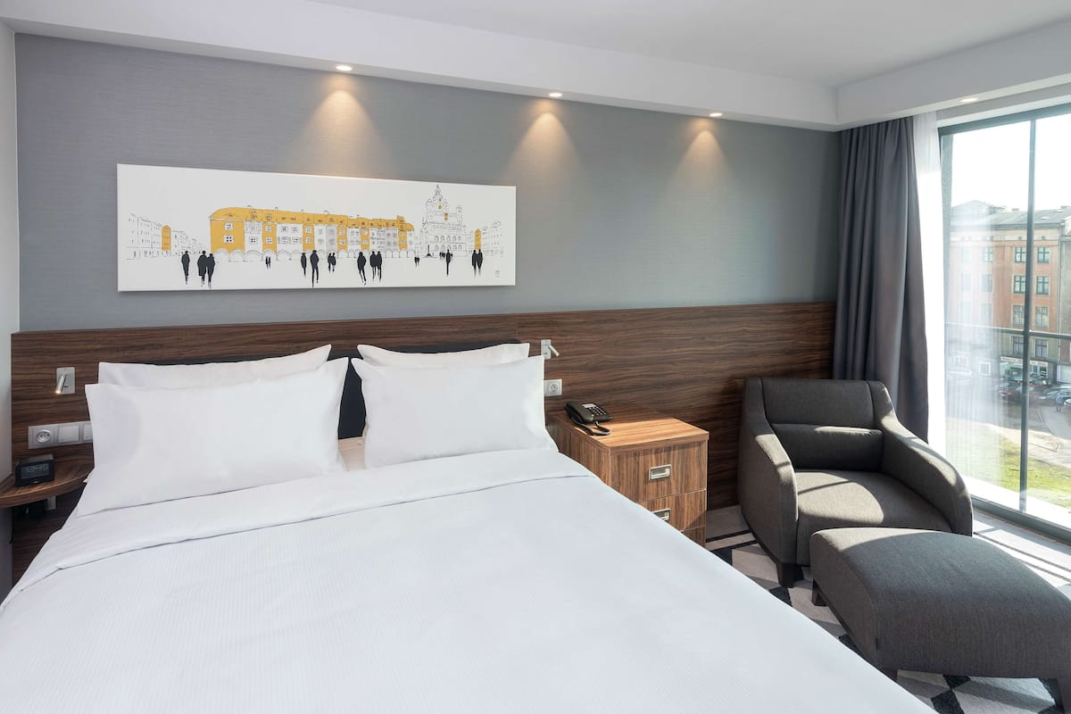 Une chambre d’hôtel avec un grand lit, une table de chevet en bois, une chaise et un tableau au mur.
