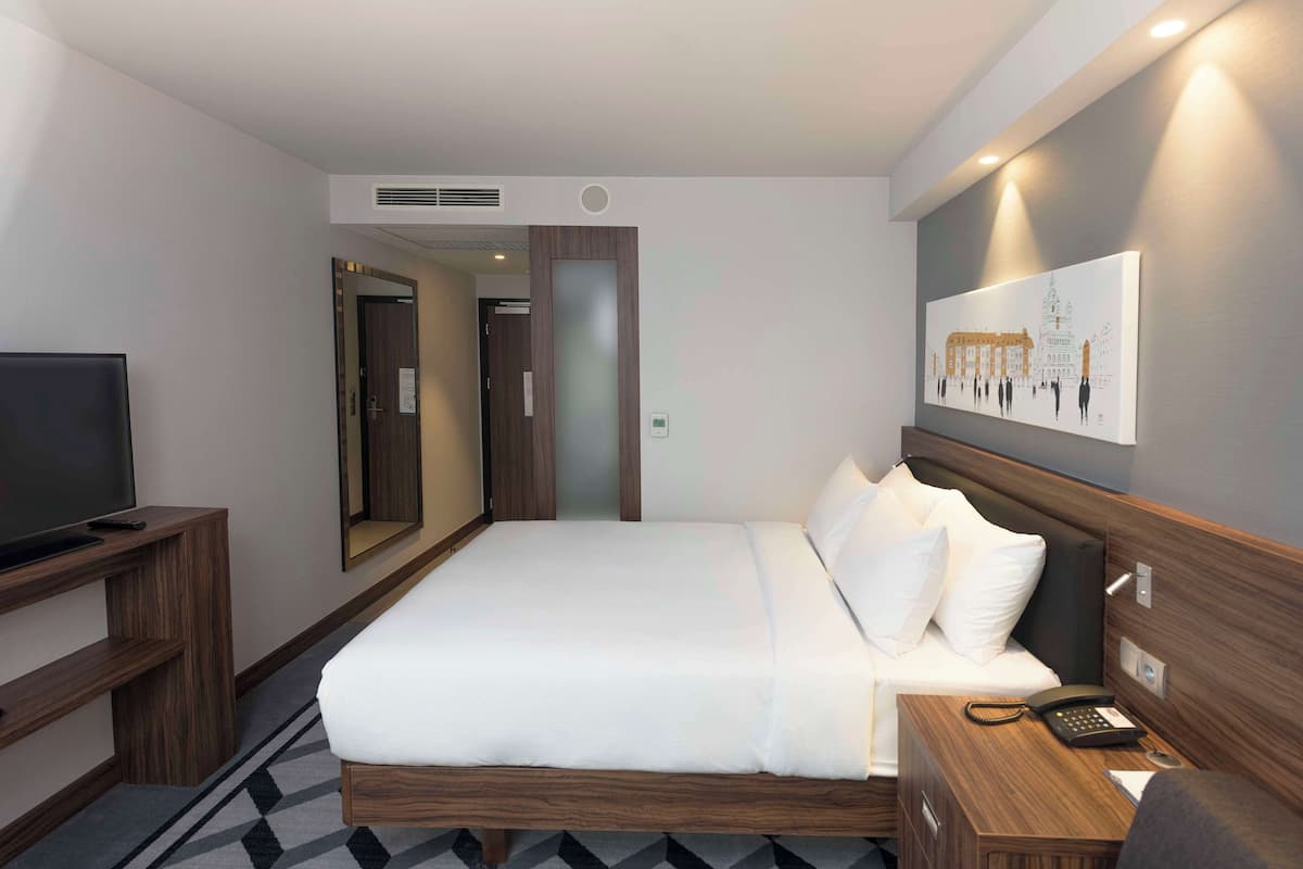 Une chambre d’hôtel avec un lit, un bureau avec un téléphone, une télévision et un tableau au mur.