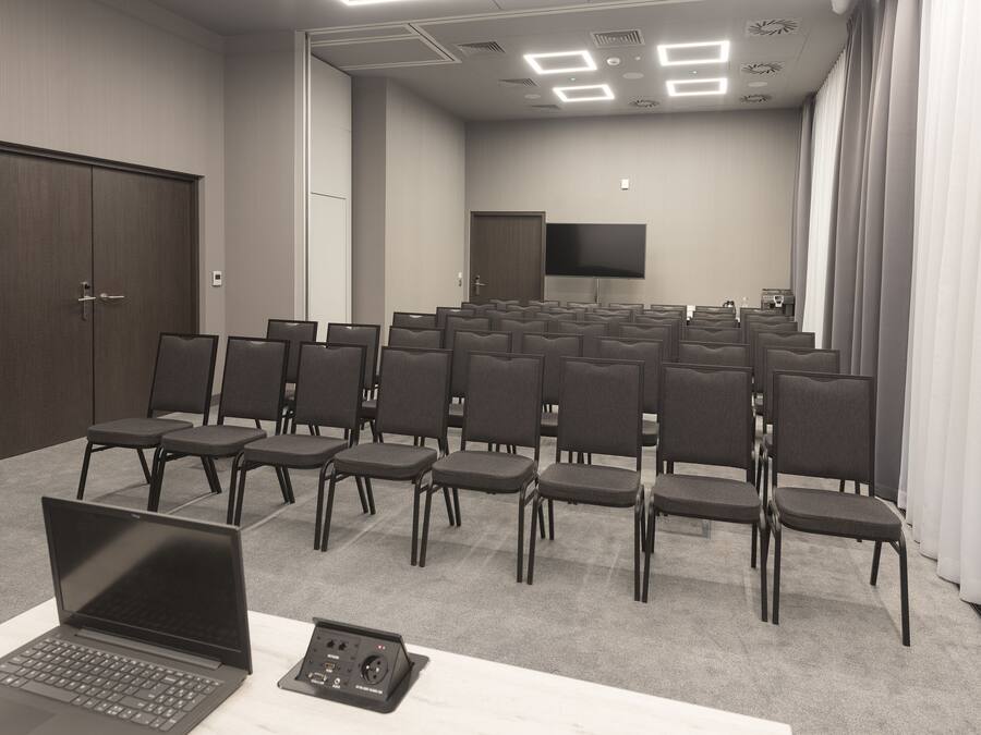 A conference room with rows of chairs, a laptop, and a projector on a table.