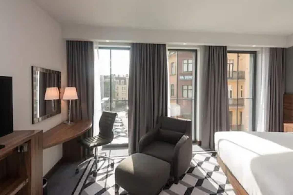 Une chambre d’hôtel avec un lit, un bureau avec une lampe, une chaise et un canapé.