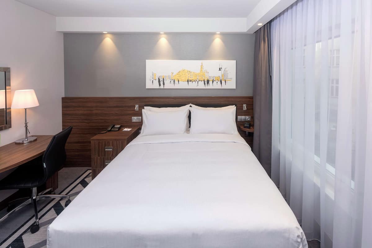 Une chambre d’hôtel avec un grand lit, un bureau avec une chaise, une lampe, un téléphone et un tableau au mur.