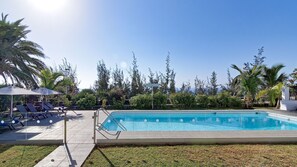 A swimming pool with lounge chairs and umbrellas, surrounded by palm trees and a clear sky.