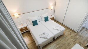 Een hotelkamer met twee bedden, een houten vloer en een wit kleurenschema.