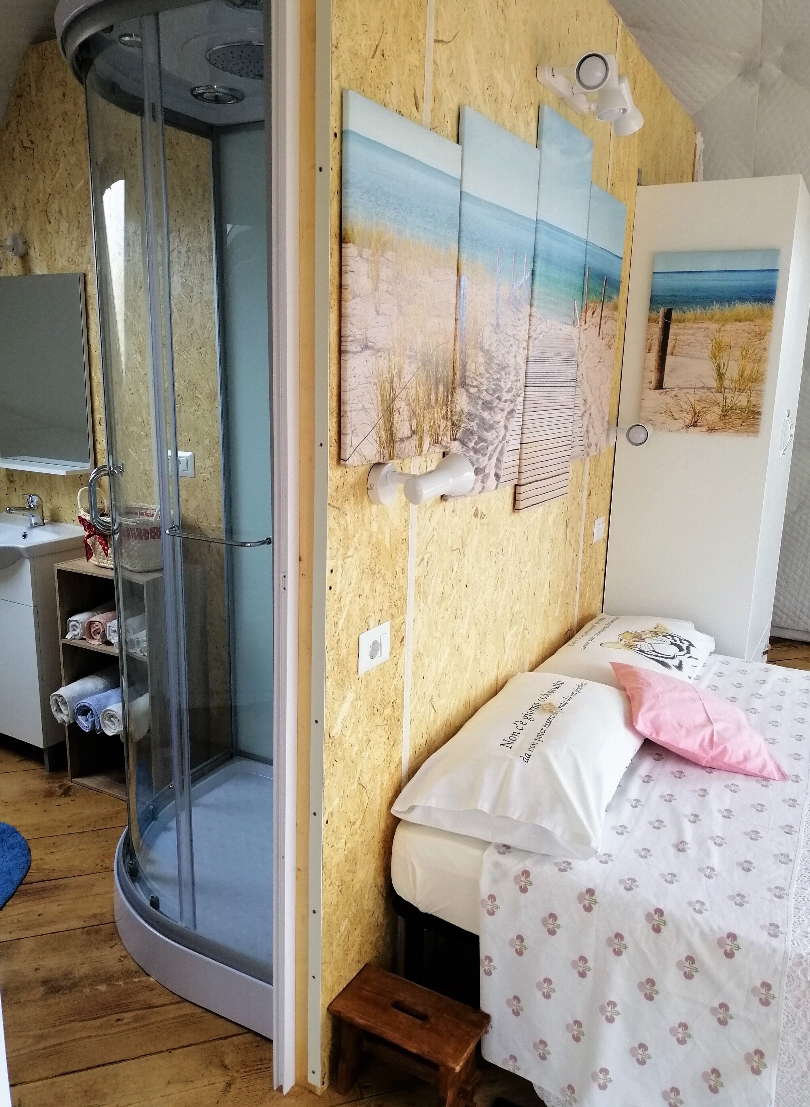 Ein Schlafzimmer mit Duschkabine mit Rundbogen, einem Bett mit gemusterten Betttextilien und einem Kunstwerk an der Wand.