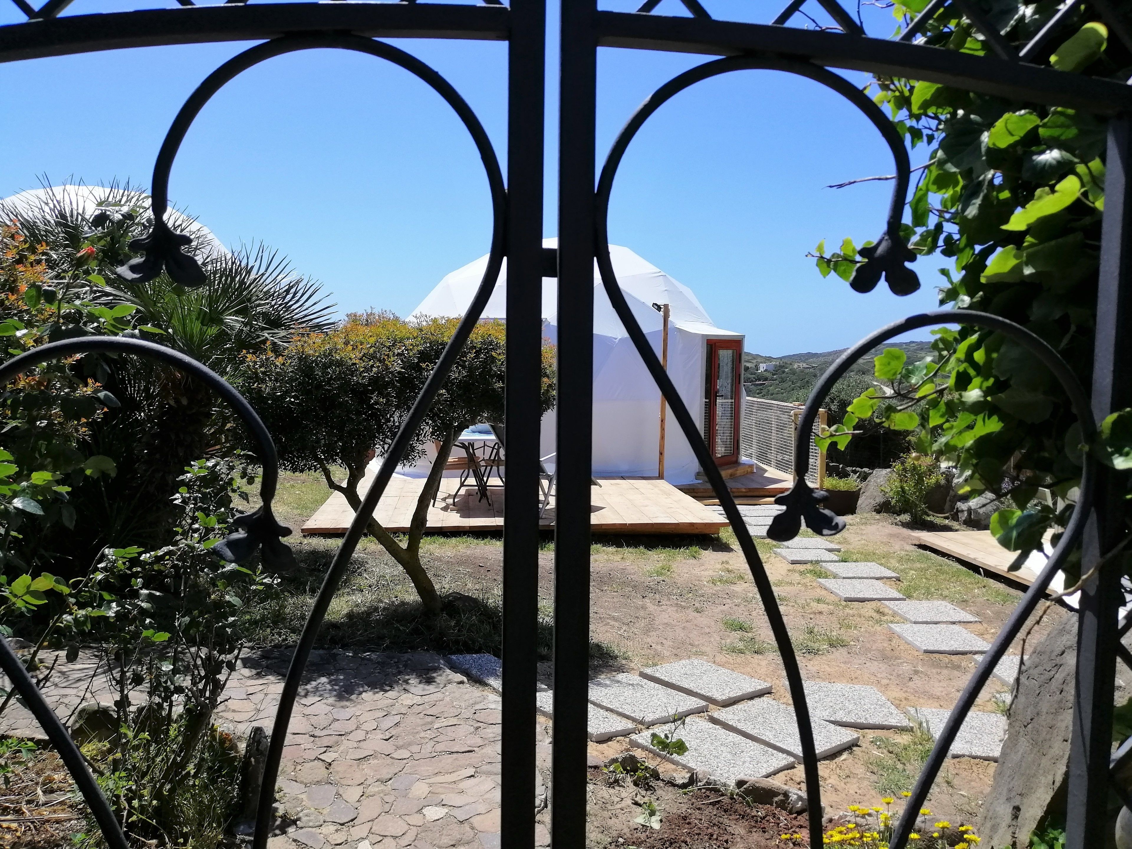 A garden pathway leading to a white tent-like structure with a wooden deck and a door.