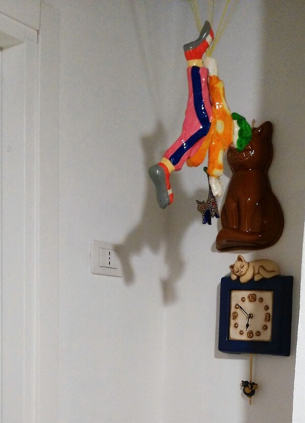 Una pared con un reloj, una figurita de gato y un adorno colgante.