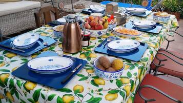 A table set outdoors with a tablecloth featuring a lemon pattern, surrounded by chairs.