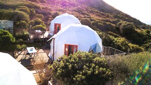 Two white dome-shaped buildings with red doors, surrounded by greenery and a hillside. - B&B Semaforo di Capo Sperone (Sant'Antioco)