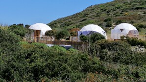 Three dome-shaped structures with a wooden fence in the foreground, set against a hillside with greenery. - B&B Semaforo di Capo Sperone (Sant'Antioco)