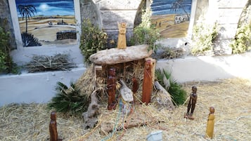 A nativity scene with a stable, figures of Mary, Joseph, baby Jesus, and animals, set against a backdrop of a mural depicting a desert landscape.