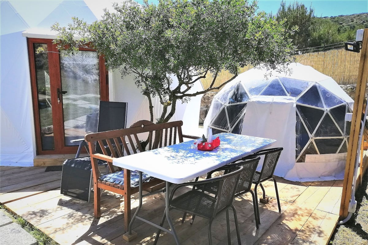 A patio with a table and chairs, a covered seating area, and a view of a tree and landscape.