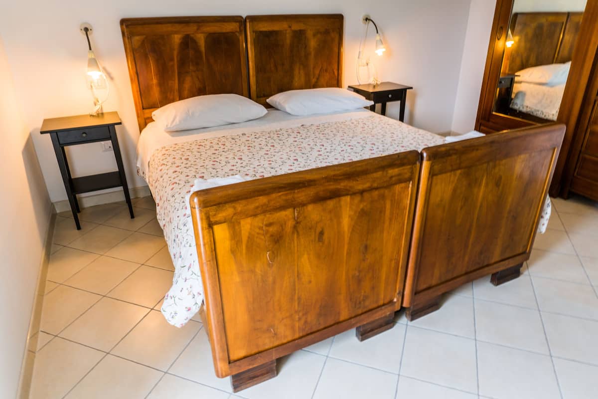 Een houten bed met hoofdeinde, twee nachtkastjes en een spiegel aan de muur.