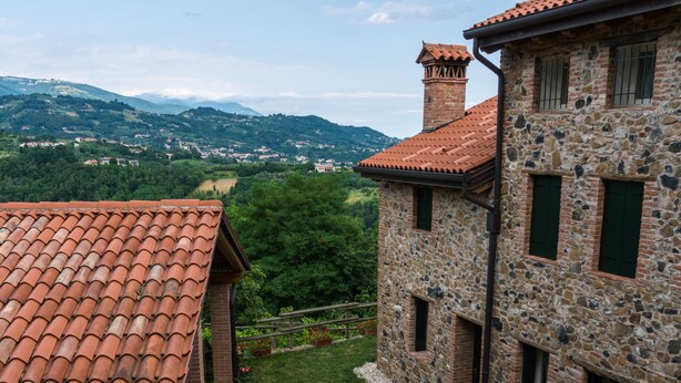 A stone building with a red-tiled roof, a chimney, and a wooden fence in the foreground.