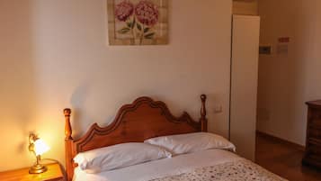 Un dormitorio con una cama de madera, ropa de cama blanca, una lámpara de noche y una obra de arte floral en la pared.