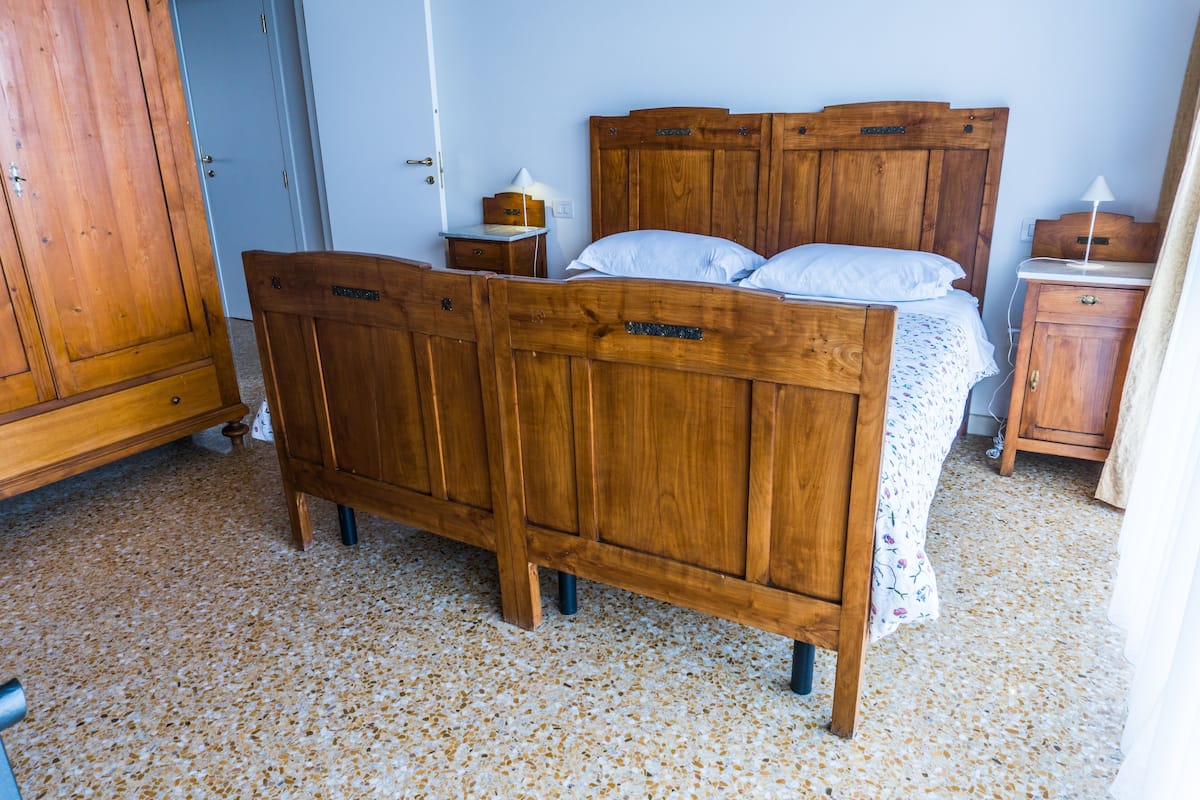 Een houten bed met hoofdeinde, een nachtkastje met lamp en een houten kledingkast.