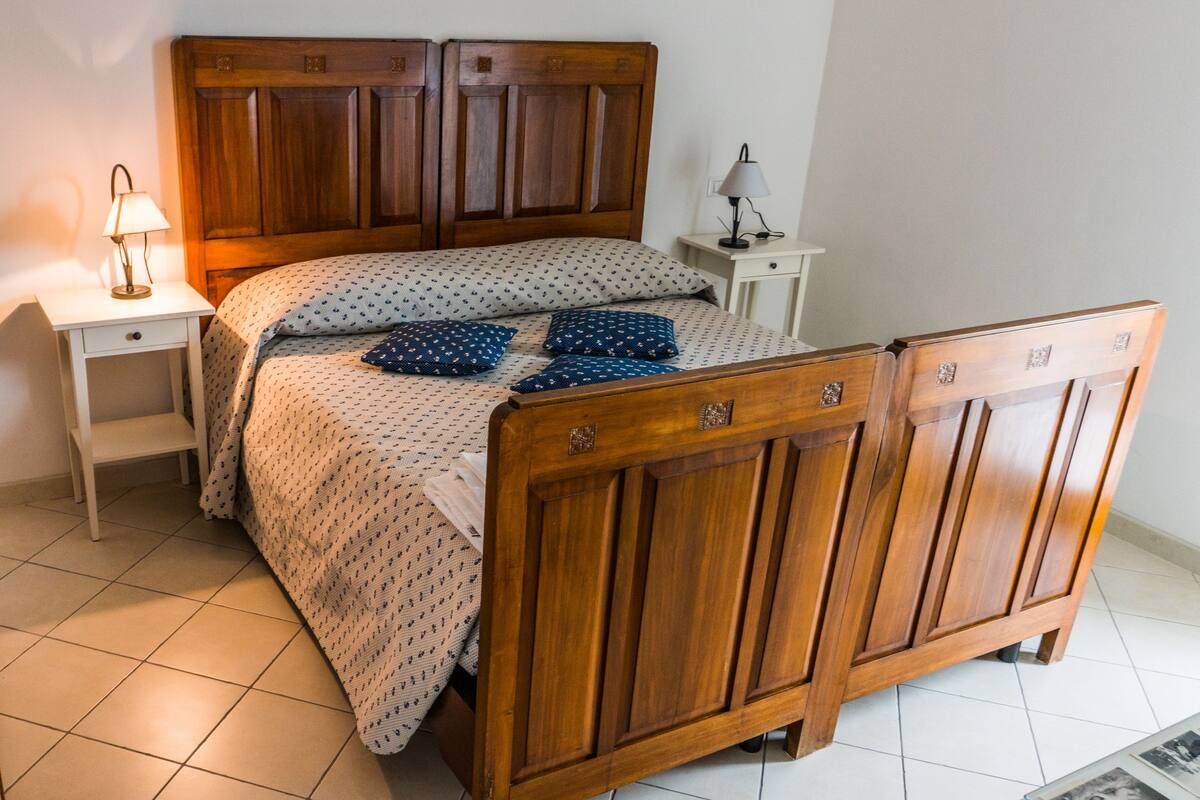 Een slaapkamer met een houten bed, nachtkastje en een lamp.