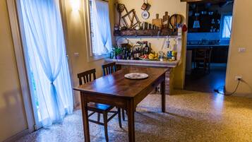 Un'area pranzo con tavolo e sedie in legno, una cucina sullo sfondo e una finestra con tende leggere.