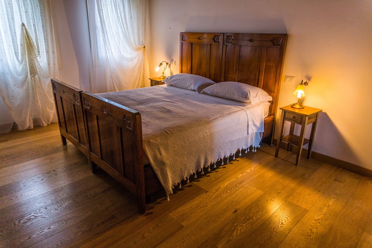 Een houten bed met hoofdeinde, twee nachtkastjes met lampen en een houten vloer.