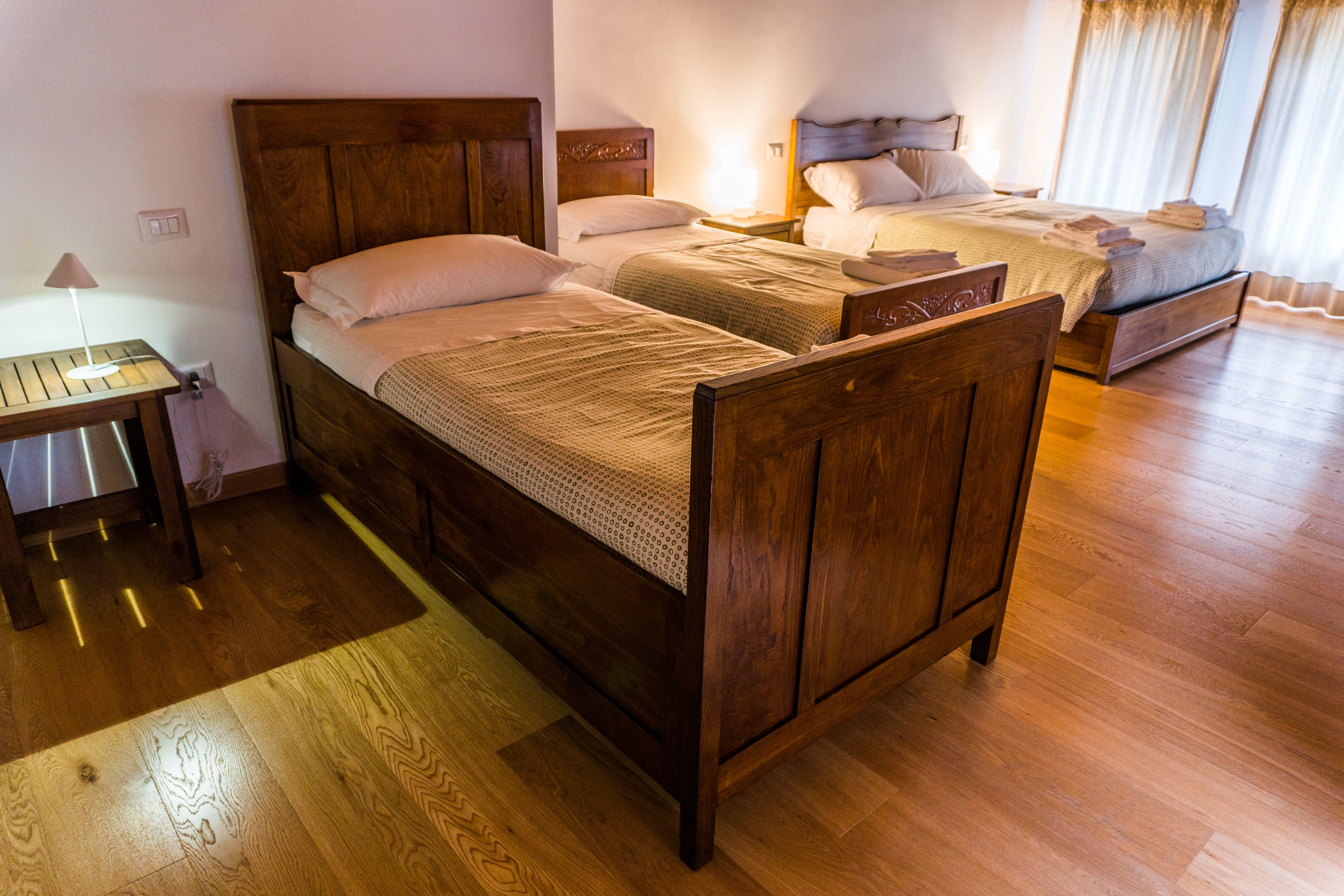 A hotel room with two wooden beds, a nightstand, and a wooden floor.