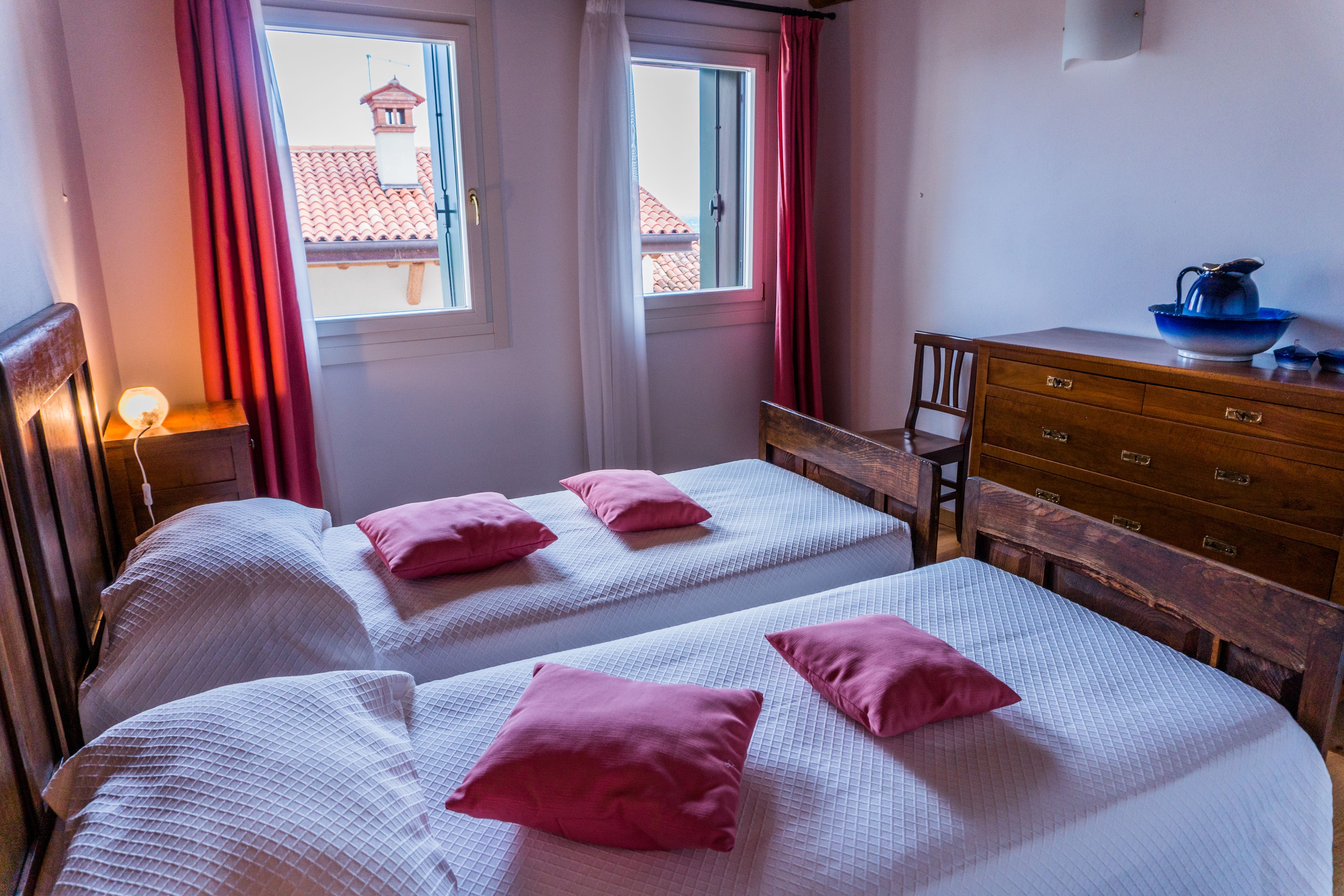 Un dormitorio con dos camas, un aparador de madera, una silla y una ventana con cortinas.