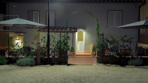 Une cour avec l’entrée d’un bâtiment, une allée couverte et des plantes en pot.