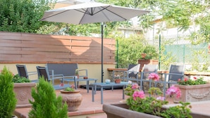 Une terrasse extérieure avec une table et des chaises en bois, un grand parasol et des plantes en pot.