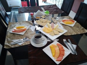 Una mesa de desayuno con platos de fruta, tostadas y una taza de café.