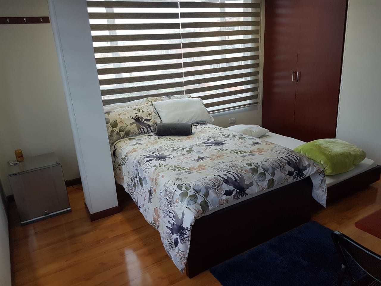 A bedroom with a bed, a nightstand, a wardrobe, and a window with blinds.
