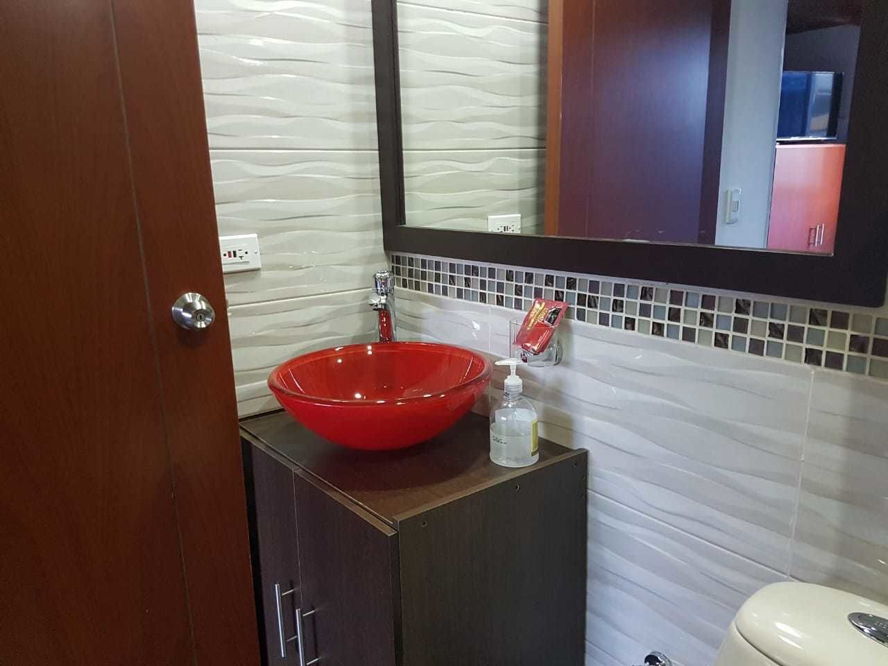 Un baño con un lavamanos de vidrio rojo, un espejo y un inodoro blanco.