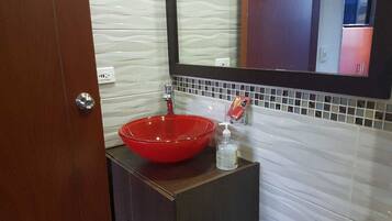 Un baño con un lavamanos de vidrio rojo, un espejo y un inodoro blanco.