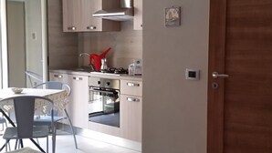 Una habitación con dos camas, una zona de cocina con armarios y una estufa, y una mesa de comedor con sillas.