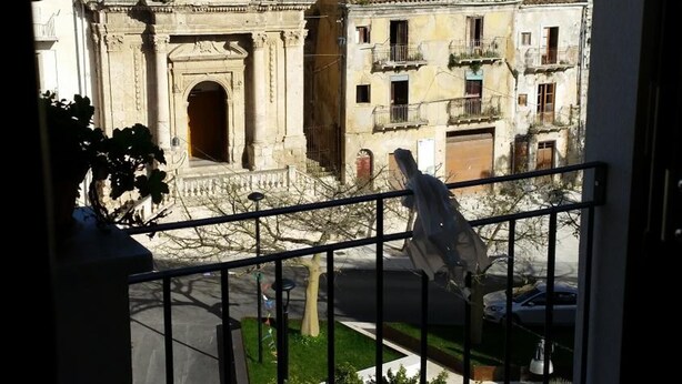 Vista de un edificio histórico con un campanario, una calle con coches aparcados y un balcón con barandilla.