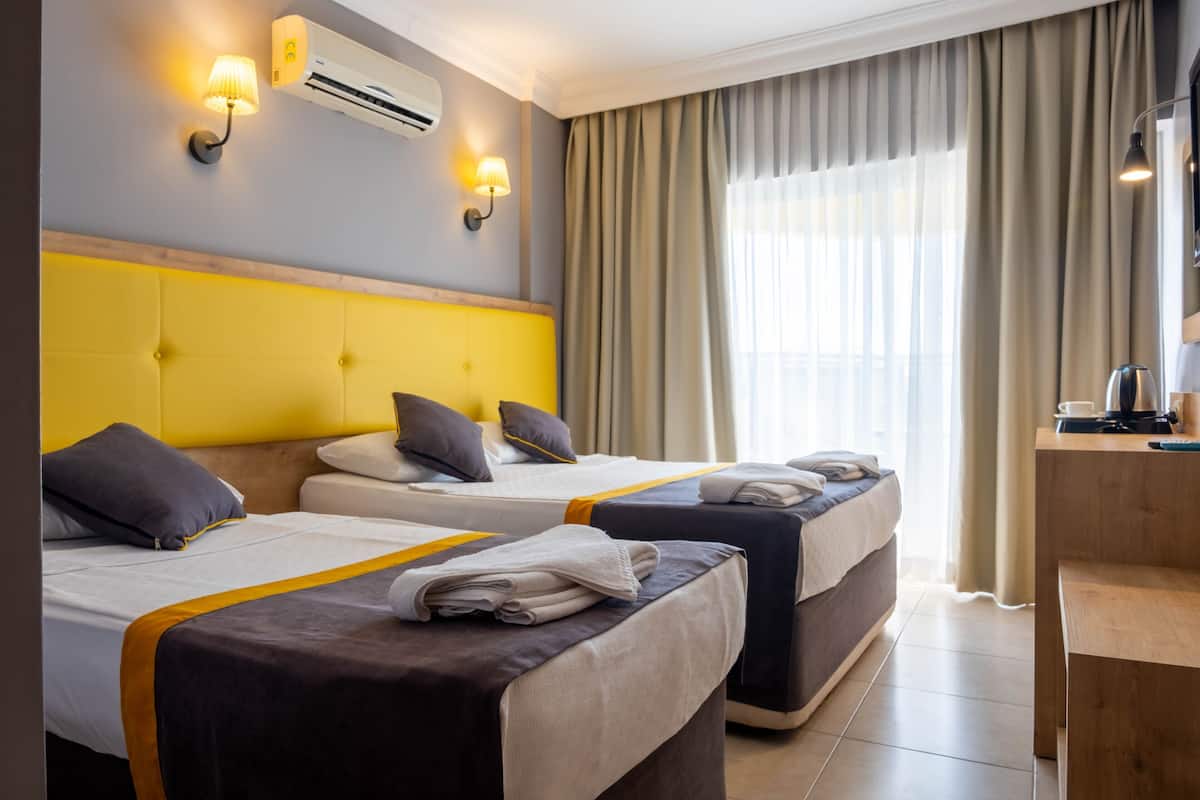A hotel room with two beds, a wooden desk, and a large window with curtains.