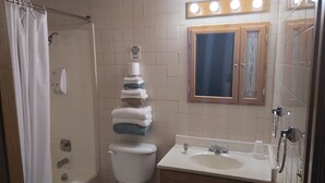 A bathroom with a toilet, sink, and shower. There is a stack of towels on the wall and a sign above the toilet. - Comfort Zone Inn (Rothsay)