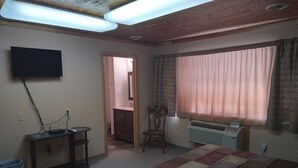 A bedroom with a bed, a desk with a computer, a TV mounted on the wall, and a window with curtains. - Comfort Zone Inn (Rothsay)
