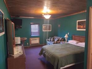 A bedroom with a bed, a television, a window with blinds, a heater, and a ceiling fan.