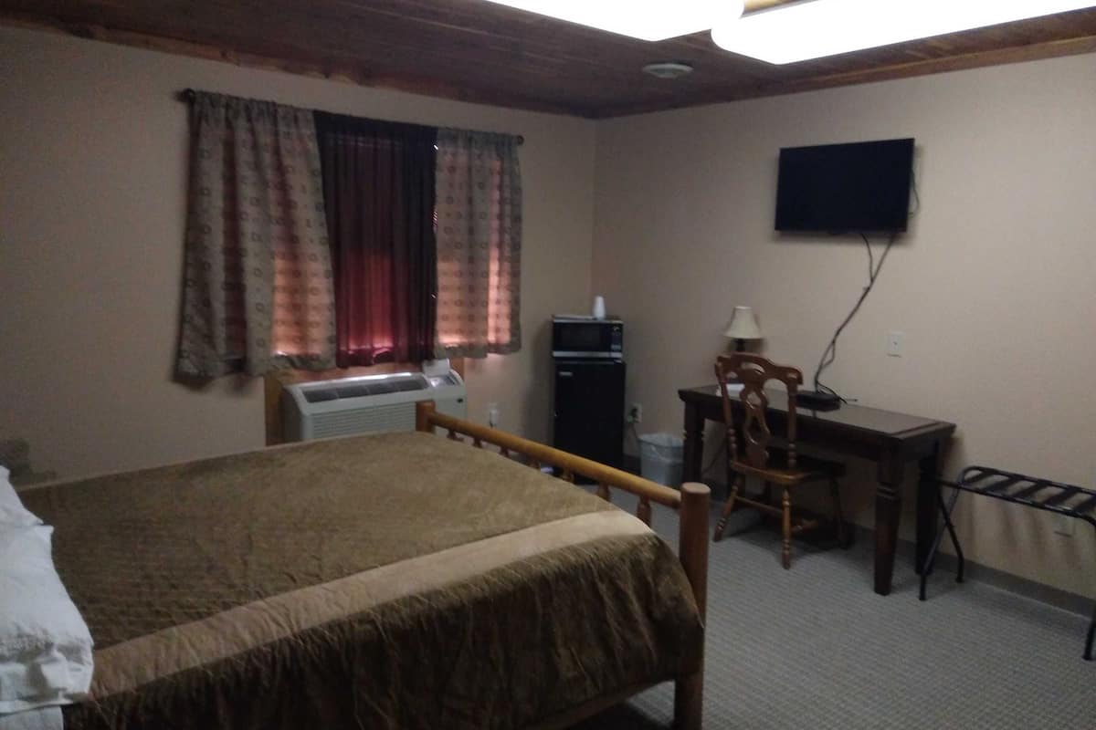 A bedroom with a bed, a desk, a chair, a television on the wall, and a window with curtains.