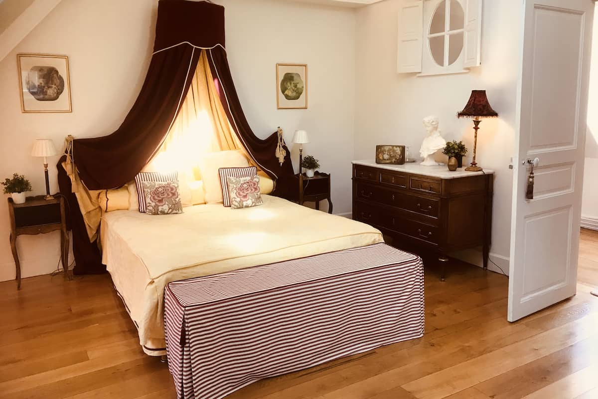 A bedroom with a canopy bed, a dresser, a nightstand, and a door.
