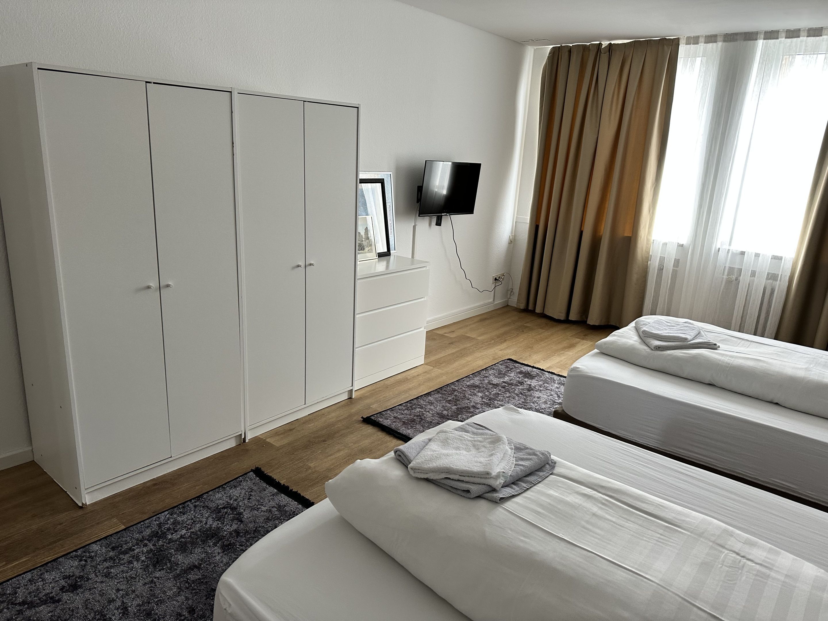 Una habitación de hotel con cama, armario, televisor y ventana con cortinas.