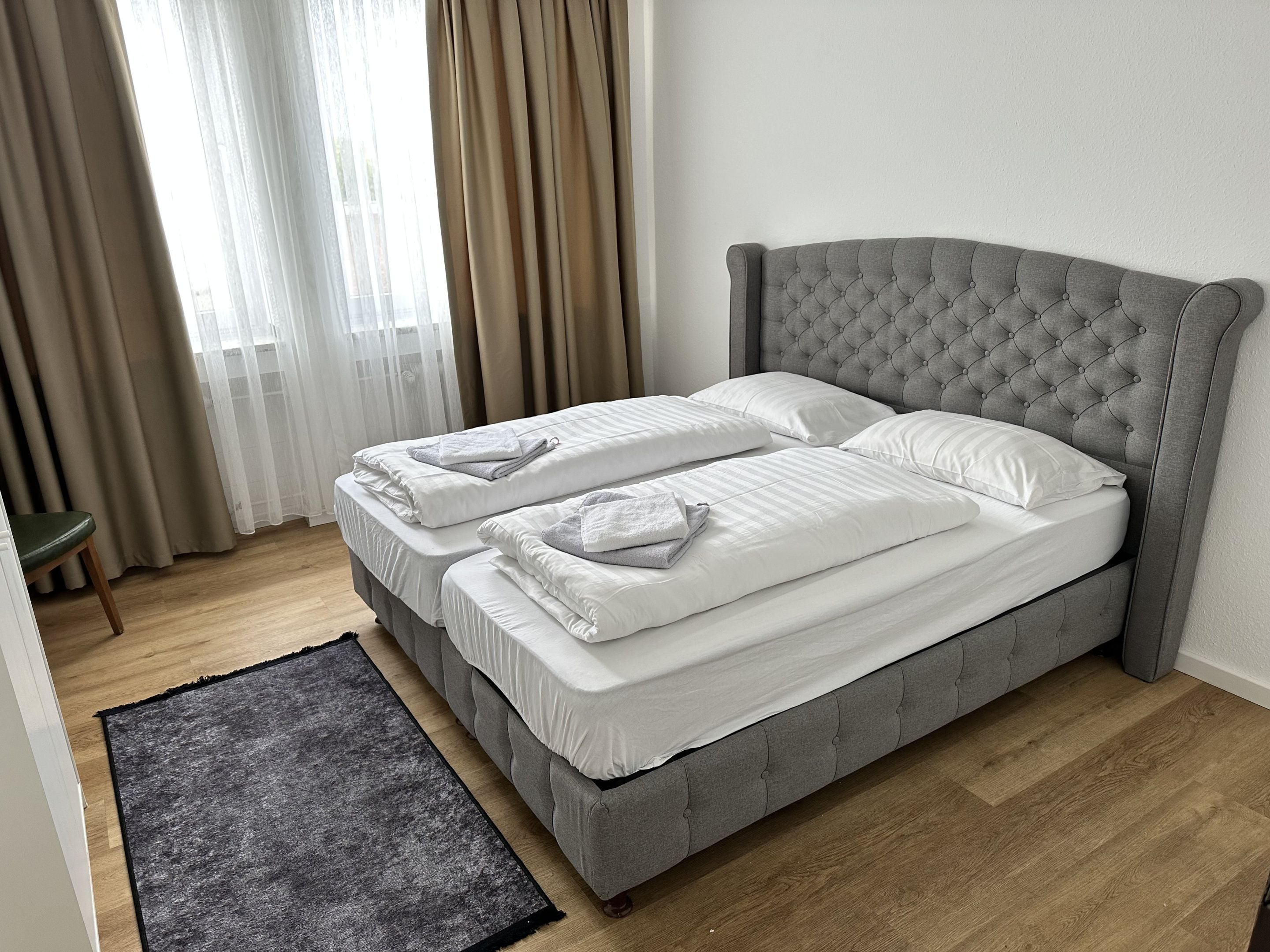 Ein Doppelbett mit einem gesteppten Kopfteil in einem Zimmer mit Holzboden und einem grauen Teppich.