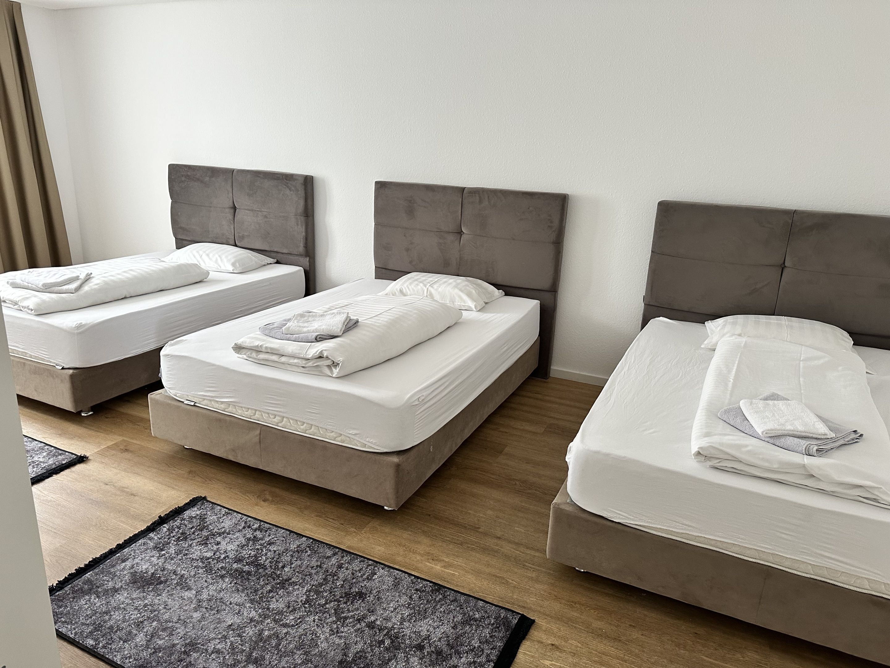 A hotel room with three beds, each with a grey headboard and white bedding.