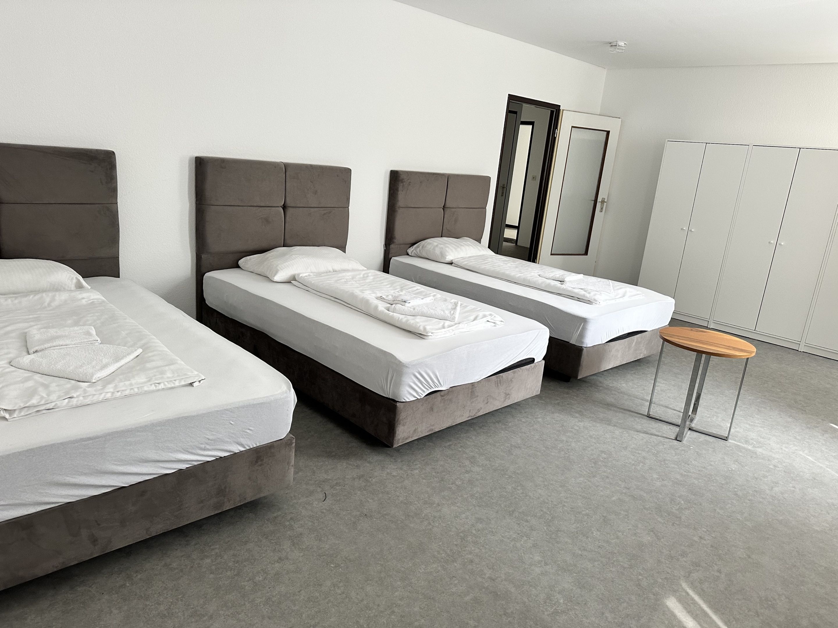 A hotel room with three beds, a small round table, and a wardrobe.