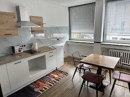 Una cocina moderna con armarios blancos, encimera de madera y estufa integrada. Hay un comedor con una mesa y sillas, y una ventana con persianas.