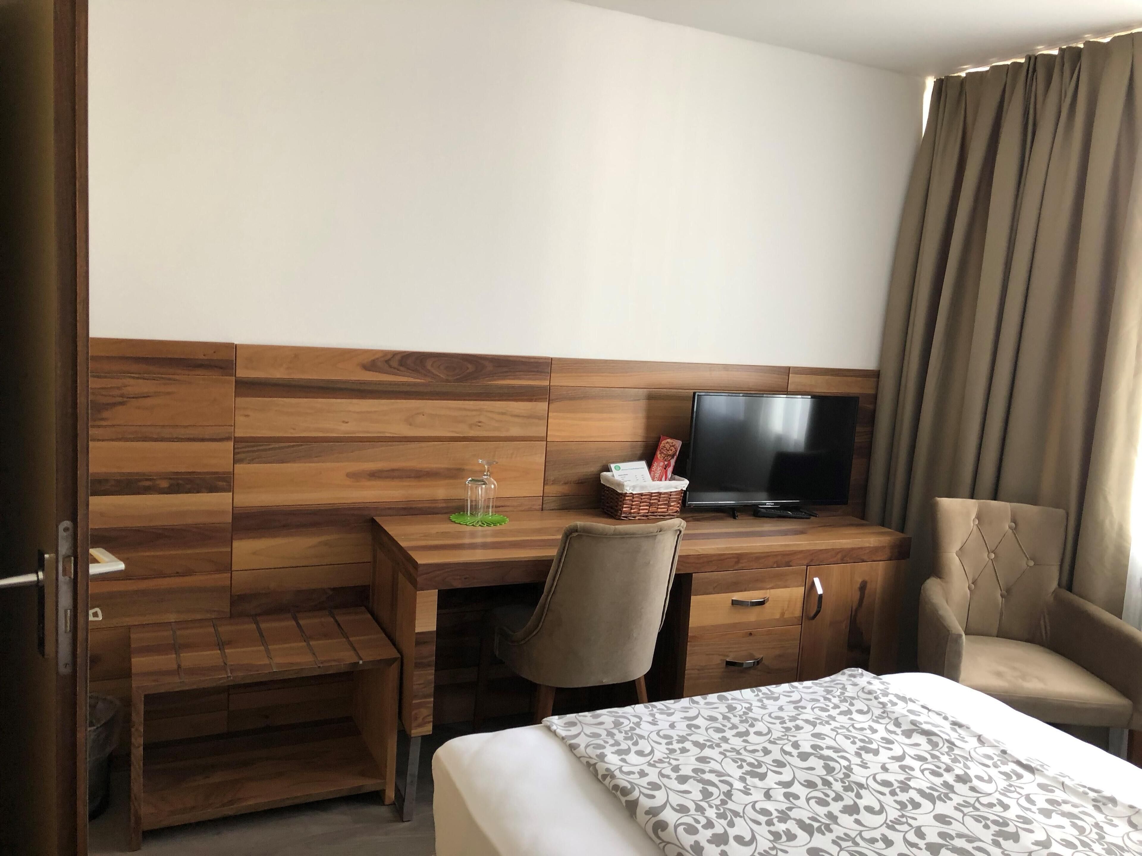 A hotel room with a wooden desk, a television, a bed with a patterned bedspread, and a chair.