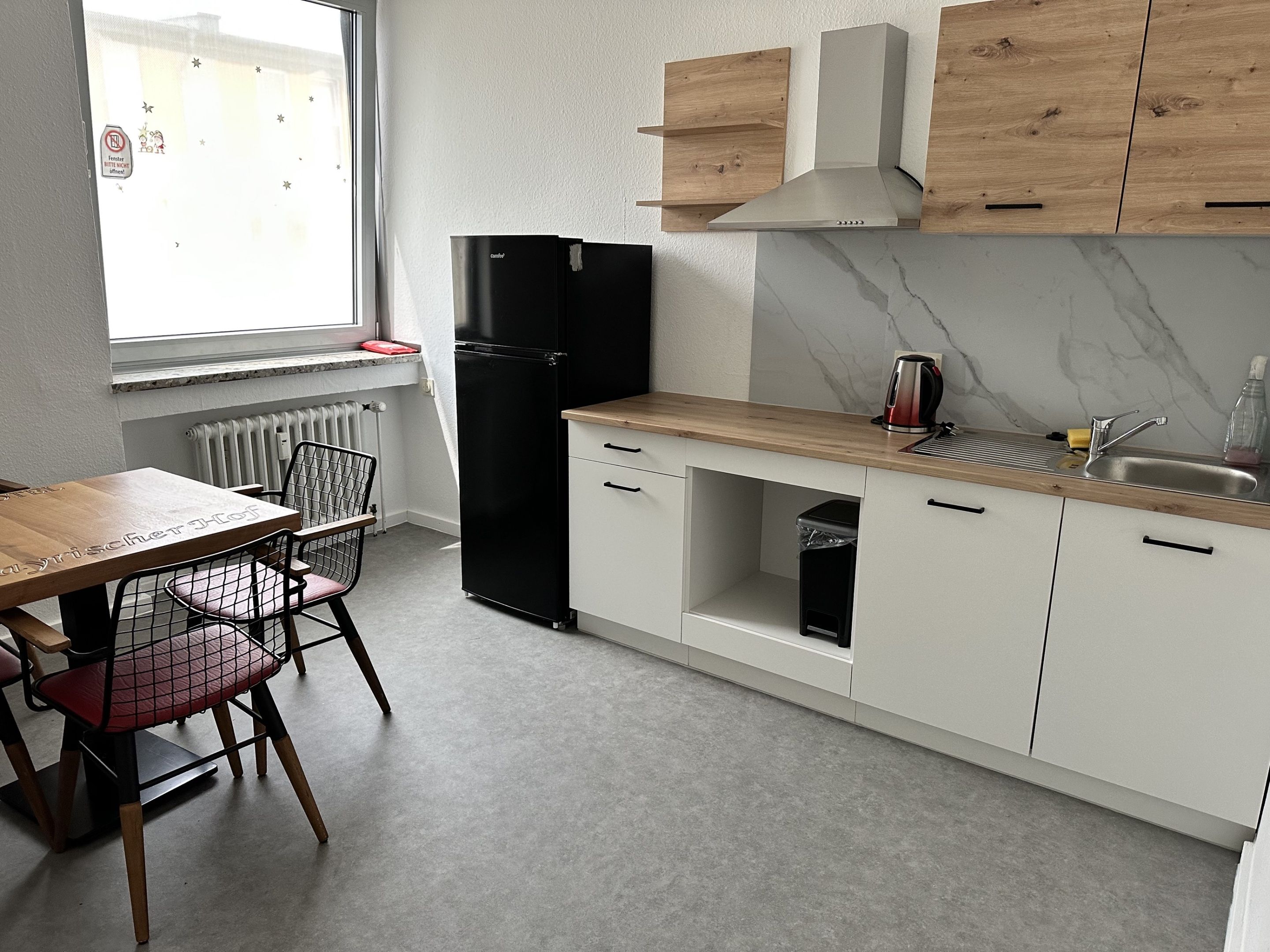 A compact kitchen with a black refrigerator, wooden cabinets, a marble backsplash, and a window with a view.