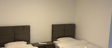 Habitación de hotel con dos camas, una mesita de noche, piso de madera y una lámpara en el techo.