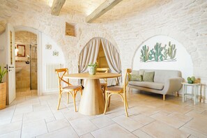 A room with a stone wall, a round wooden table with chairs, a sofa, and a cactus wall art piece. - Trulli Di Zia Vittoria (Alberobello)