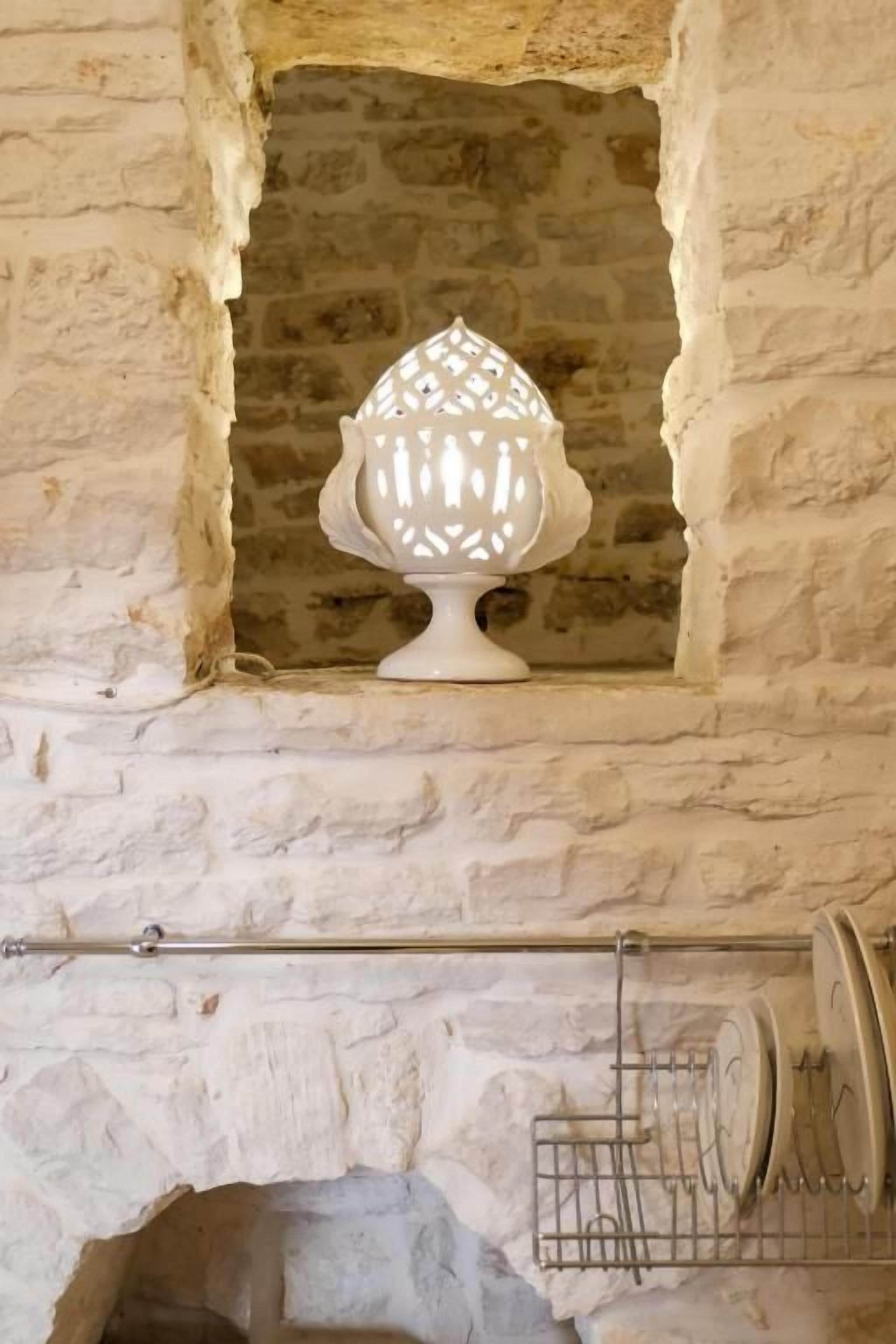 En hvid keramisk lampe med geometrisk design i en niche med stensramme.